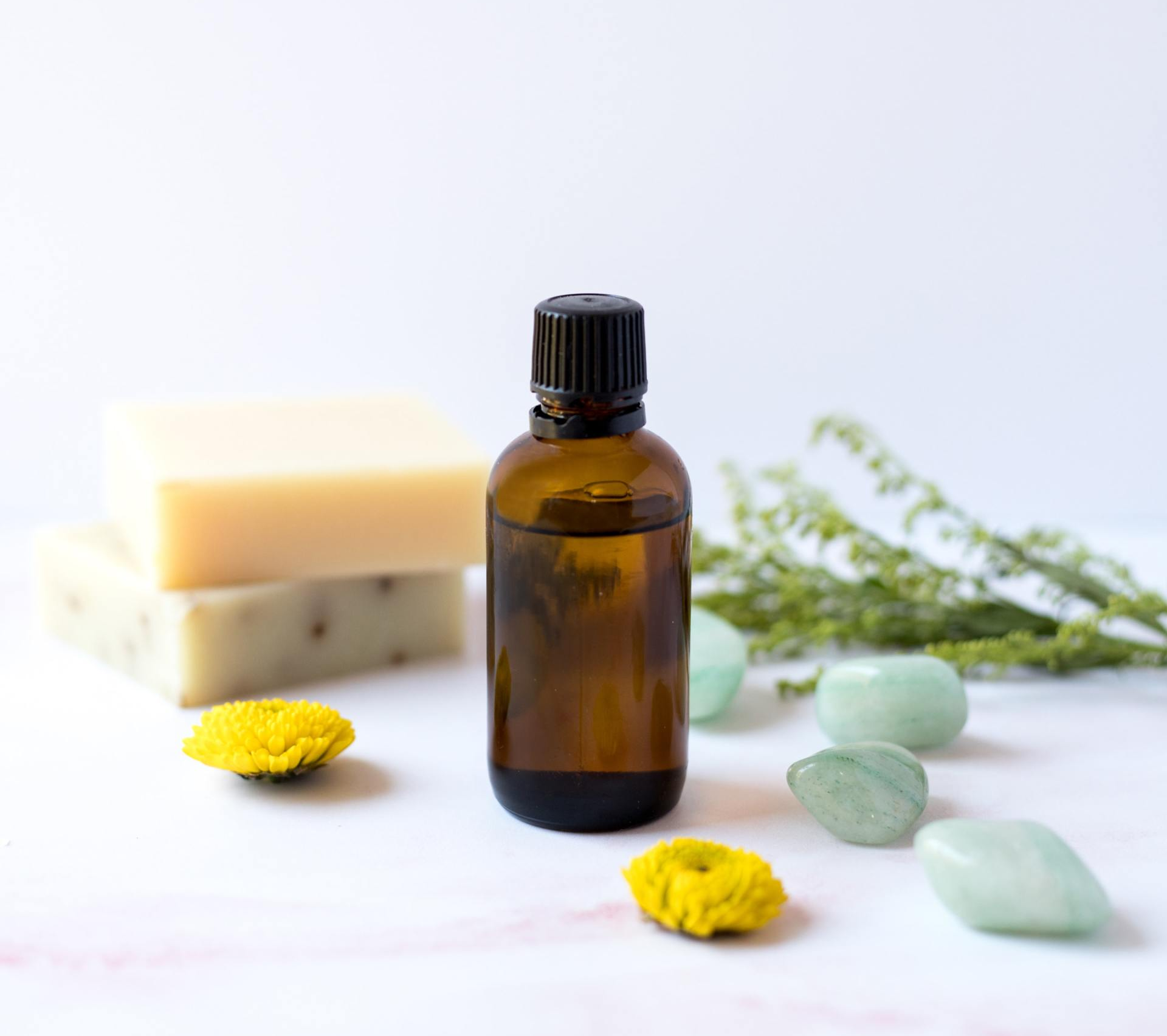 Amber bottle with soap bars, yellow flowers, and green stones on a white background