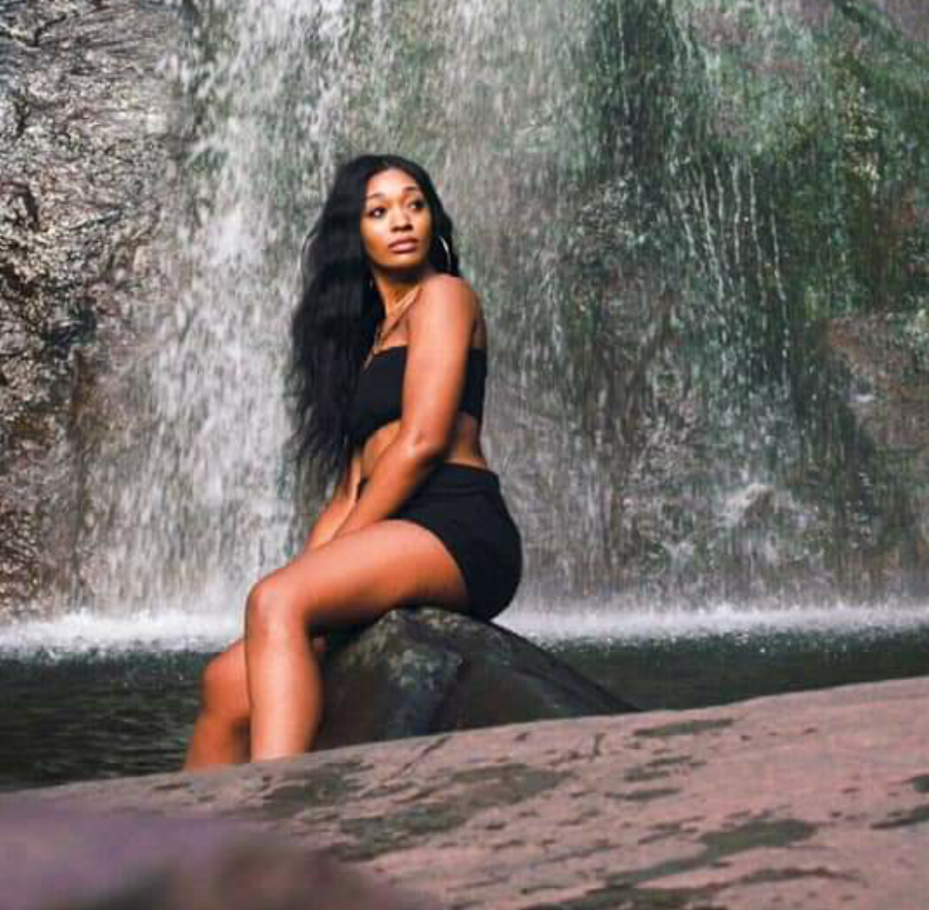 Woman in a black dress sitting on a rock in front of a waterfall